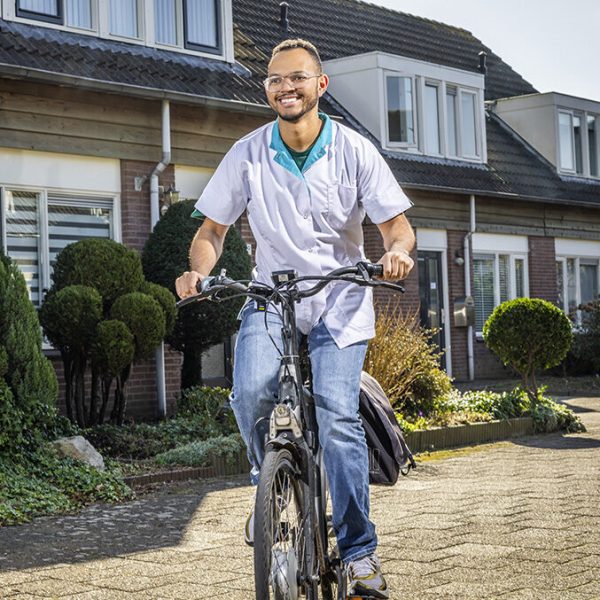 Verpleger op een elektrische fiets fiets door de woonwijk met brede lach op het gezicht